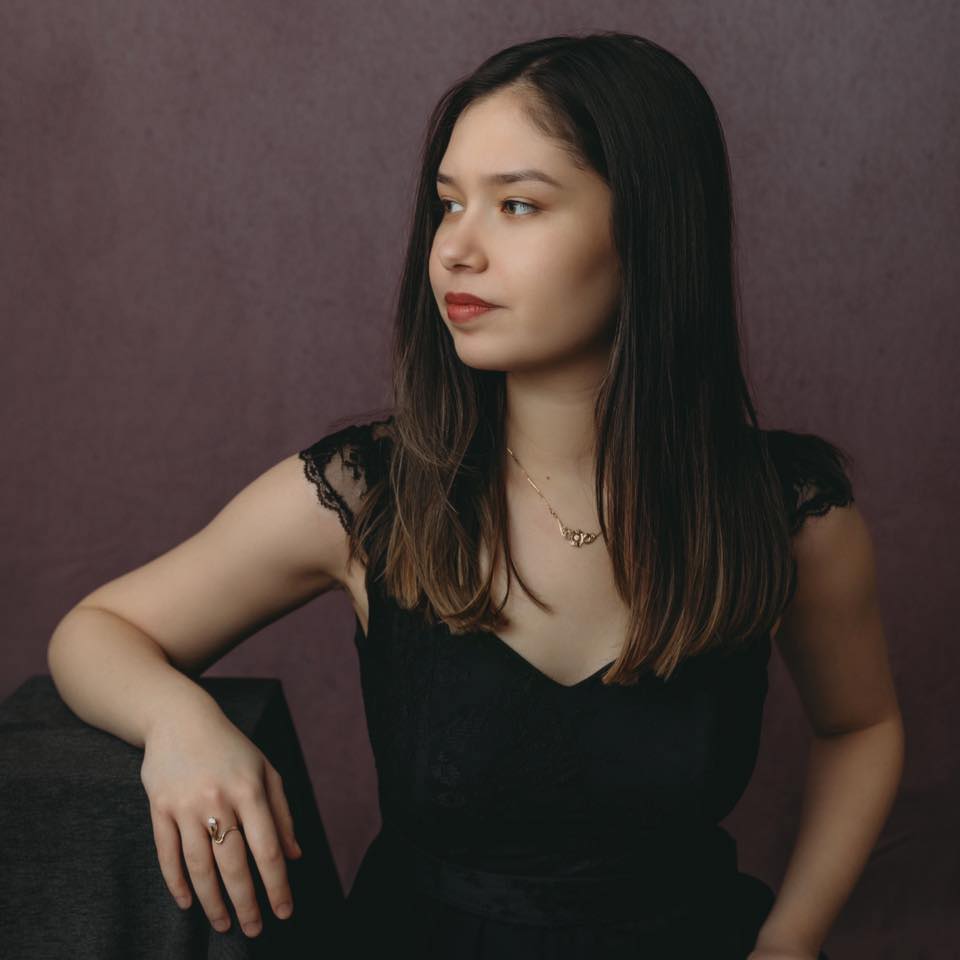 a person in a black dress looking to the left in front of a gray wall